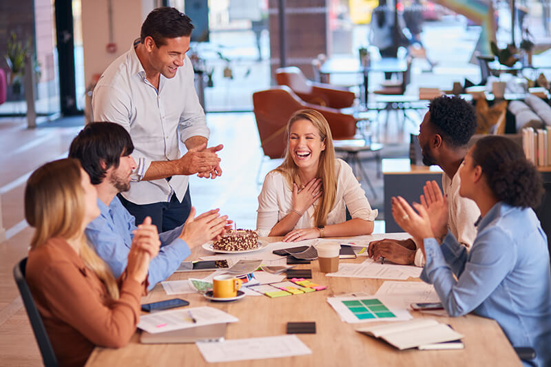 office person given surpise cake around table shutterstock 1979672885